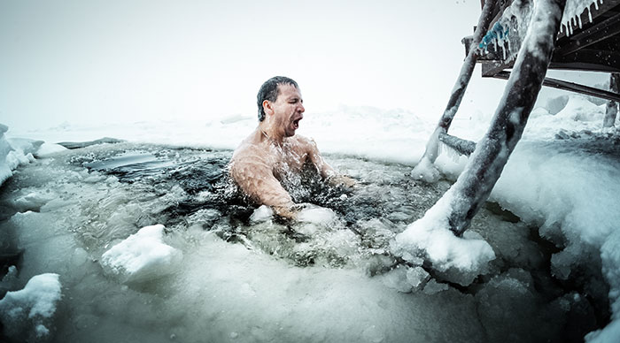 Young man swimming in the ice hole on a winter lake in Finland
